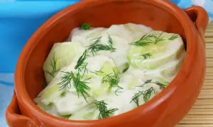 Mizeria przepis: świeże plasterki ogórka w kremowym sosie jogurtowym z koperkiem, podane w glinianej miseczce.