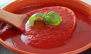 Gęsty, domowy ketchup z pomidorów malinowych, z listkiem bazylii na drewnianej łyżce.