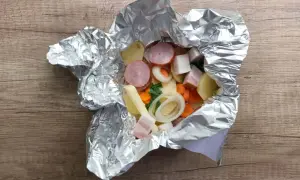 Gotowe do grillowania: ziemniaki z grilla w folii z kiełbasą, boczkiem i warzywami. Pyszny posiłek wprost z ogniska.