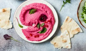 Piękny, różowy hummus z buraka, udekorowany kwiatkiem i granatem, podany z pitą.