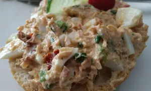 Pyszna pasta z tuńczyka z jajkiem i szczypiorkiem na bułce, ozdobiona plasterkiem ogórka i pomidorkiem.