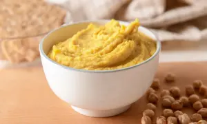 Puszysta pasta z ciecierzycy w miseczce, obok kilka ziaren ciecierzycy i chrupki.