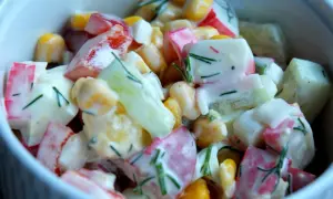 Pyszna sałatka z surimi, kukurydzy, ogórka i jajka, polana kremowym sosem i posypana koperkiem.