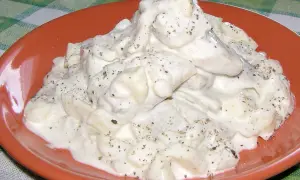 Pyszne śledzie w śmietanie, doprawione pieprzem, na pomarańczowym talerzu.
