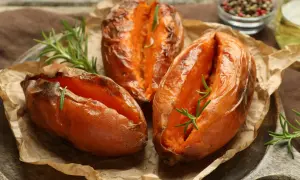 Trzy pieczone bataty z rozmarynem na papierze do pieczenia, wyglądają apetycznie i aromatycznie.