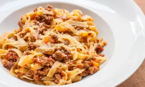 Pyszny makaron tagliatelle z bogatym sosem bolognese, posypany parmezanem. Idealny przepis na obiad.