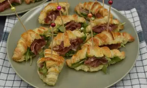 Pyszne rogaliki z ciasta francuskiego z szynką parmeńską i rukolą, podane na talerzu.
