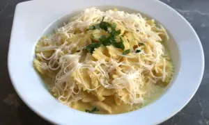Pyszne farfalle w kremowym sosie z kawałkami gotowanego kurczaka, posypane startym serem i natką pietruszki. Idealny pomysł, co zrobić z gotowanego kurczaka.