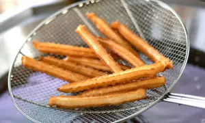 Churros przepis: złociste, chrupiące paluszki wyjęte z frytownicy na metalowej łyżce cedzakowej.