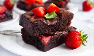 Dwa pyszne brownie z truskawkami, polane czekoladą i ozdobione świeżymi owocami i miętą. Idealne na deser.