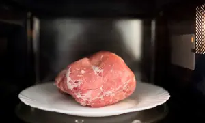 Zamrożony kawałek mięsa na talerzu w mikrofalówce. Szybki sposób, jak rozmrozić mięso, gdy brakuje czasu.
