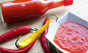 Pikantny sos z ostrej papryki w butelce i miseczce, obok świeże papryczki chili.