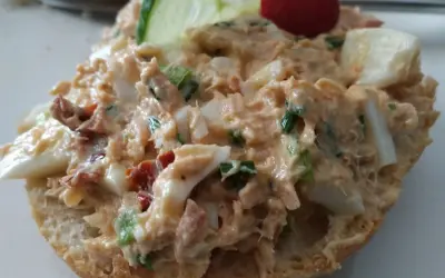 Pyszna pasta z tuńczyka z jajkiem i szczypiorkiem na bułce, ozdobiona plasterkiem ogórka i pomidorkiem.