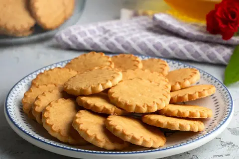 Stos pysznych, złotych kruche ciastka na talerzu z niebieskim wzorem. Idealne na popołudniową herbatkę.