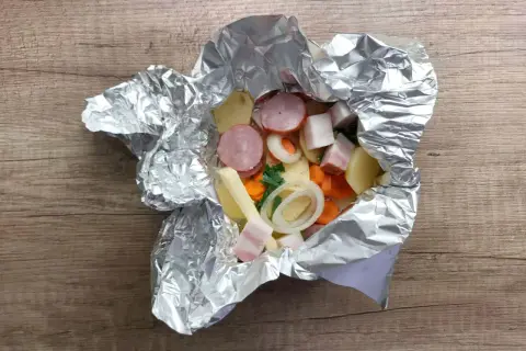 Gotowe do grillowania: ziemniaki z grilla w folii z kiełbasą, boczkiem i warzywami. Pyszny posiłek wprost z ogniska.