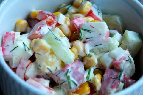 Pyszna sałatka z surimi, kukurydzy, ogórka i jajka, polana kremowym sosem i posypana koperkiem.