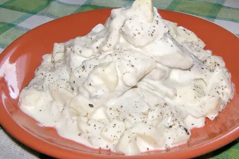 Pyszne śledzie w śmietanie, doprawione pieprzem, na pomarańczowym talerzu.