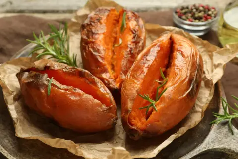 Trzy pieczone bataty z rozmarynem na papierze do pieczenia, wyglądają apetycznie i aromatycznie.