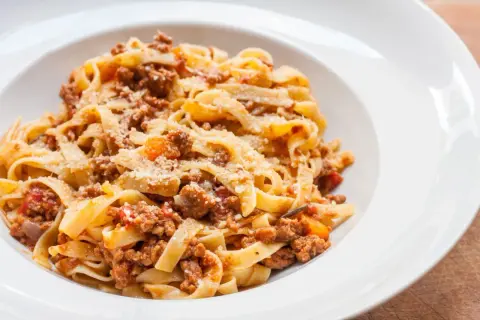 Pyszny makaron tagliatelle z bogatym sosem bolognese, posypany parmezanem. Idealny przepis na obiad.