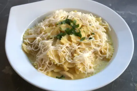 Pyszne farfalle w kremowym sosie z kawałkami gotowanego kurczaka, posypane startym serem i natką pietruszki. Idealny pomysł, co zrobić z gotowanego kurczaka.
