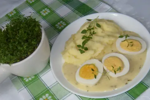 Pyszne puree ziemniaczane z jajkami w sosie chrzanowym, udekorowane świeżym tymiankiem. Obok doniczka z rzeżuchą.