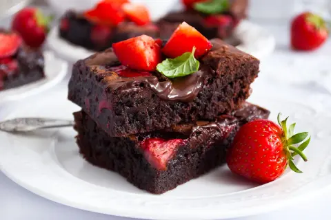 Dwa pyszne brownie z truskawkami, polane czekoladą i ozdobione świeżymi owocami i miętą. Idealne na deser.