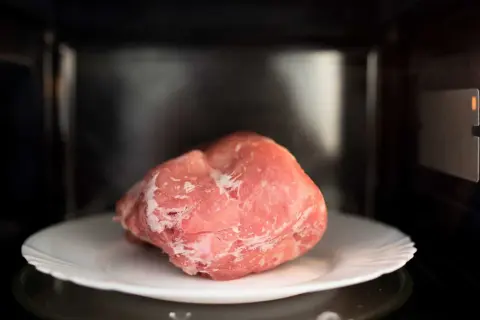 Zamrożony kawałek mięsa na talerzu w mikrofalówce. Szybki sposób, jak rozmrozić mięso, gdy brakuje czasu.
