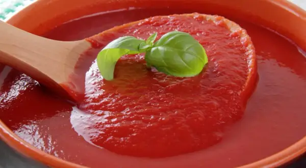 Gęsty, domowy ketchup z pomidorów malinowych, z listkiem bazylii na drewnianej łyżce.
