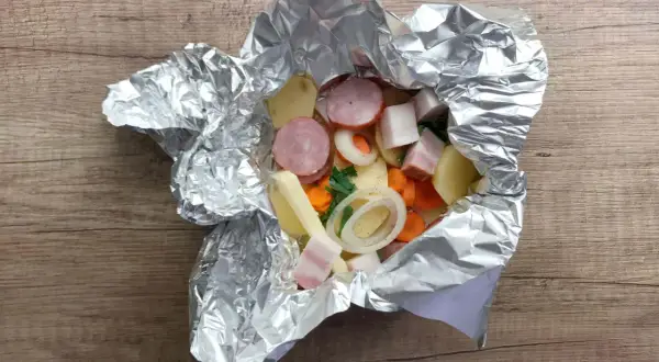 Gotowe do grillowania: ziemniaki z grilla w folii z kiełbasą, boczkiem i warzywami. Pyszny posiłek wprost z ogniska.