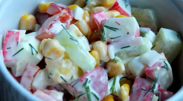 Pyszna sałatka z surimi, kukurydzy, ogórka i jajka, polana kremowym sosem i posypana koperkiem.