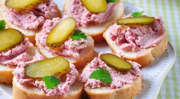 Pyszna pasta na kanapki z ogórkiem kiszonym i natką pietruszki, ułożona na kromkach chleba.