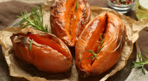 Trzy pieczone bataty z rozmarynem na papierze do pieczenia, wyglądają apetycznie i aromatycznie.