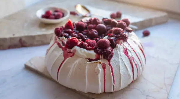 Jak piec beze? Puszysta Pavlova z kremem i wiśniami, ozdobiona syropem. Idealna na deser.