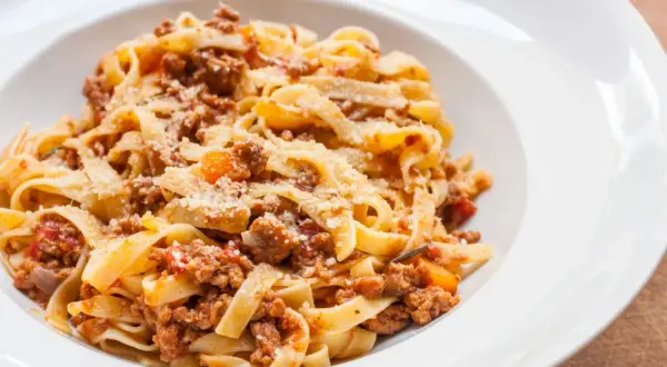 Pyszny makaron tagliatelle z bogatym sosem bolognese, posypany parmezanem. Idealny przepis na obiad.