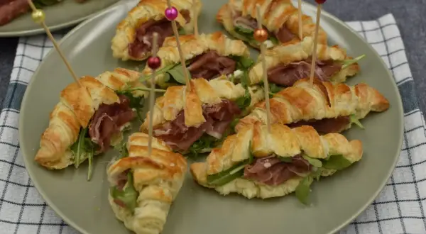 Pyszne rogaliki z ciasta francuskiego z szynką parmeńską i rukolą, podane na talerzu.