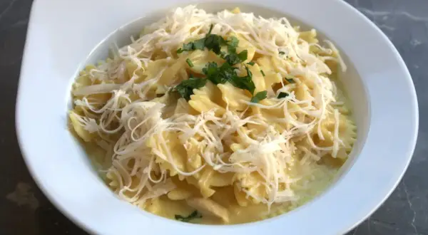 Pyszne farfalle w kremowym sosie z kawałkami gotowanego kurczaka, posypane startym serem i natką pietruszki. Idealny pomysł, co zrobić z gotowanego kurczaka.