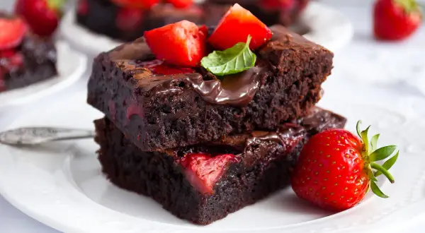 Dwa pyszne brownie z truskawkami, polane czekoladą i ozdobione świeżymi owocami i miętą. Idealne na deser.