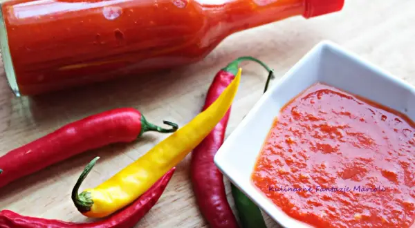 Pikantny sos z ostrej papryki w butelce i miseczce, obok świeże papryczki chili.