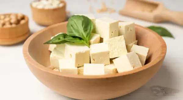 Kostki tofu w misce, ozdobione listkiem bazylii. Czy tofu można jeść na surowo? Tak, to świetna baza do sałatek.