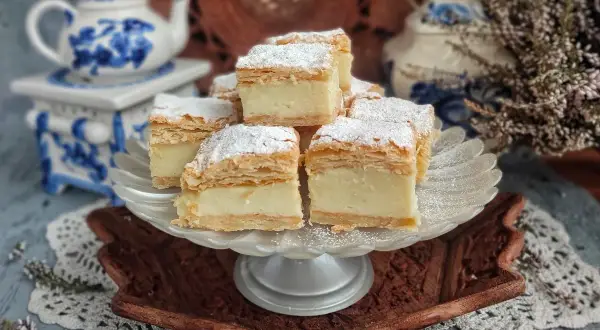 Kremowe napoleon ciasto, posypane cukrem pudrem, prezentuje się apetycznie na paterze.