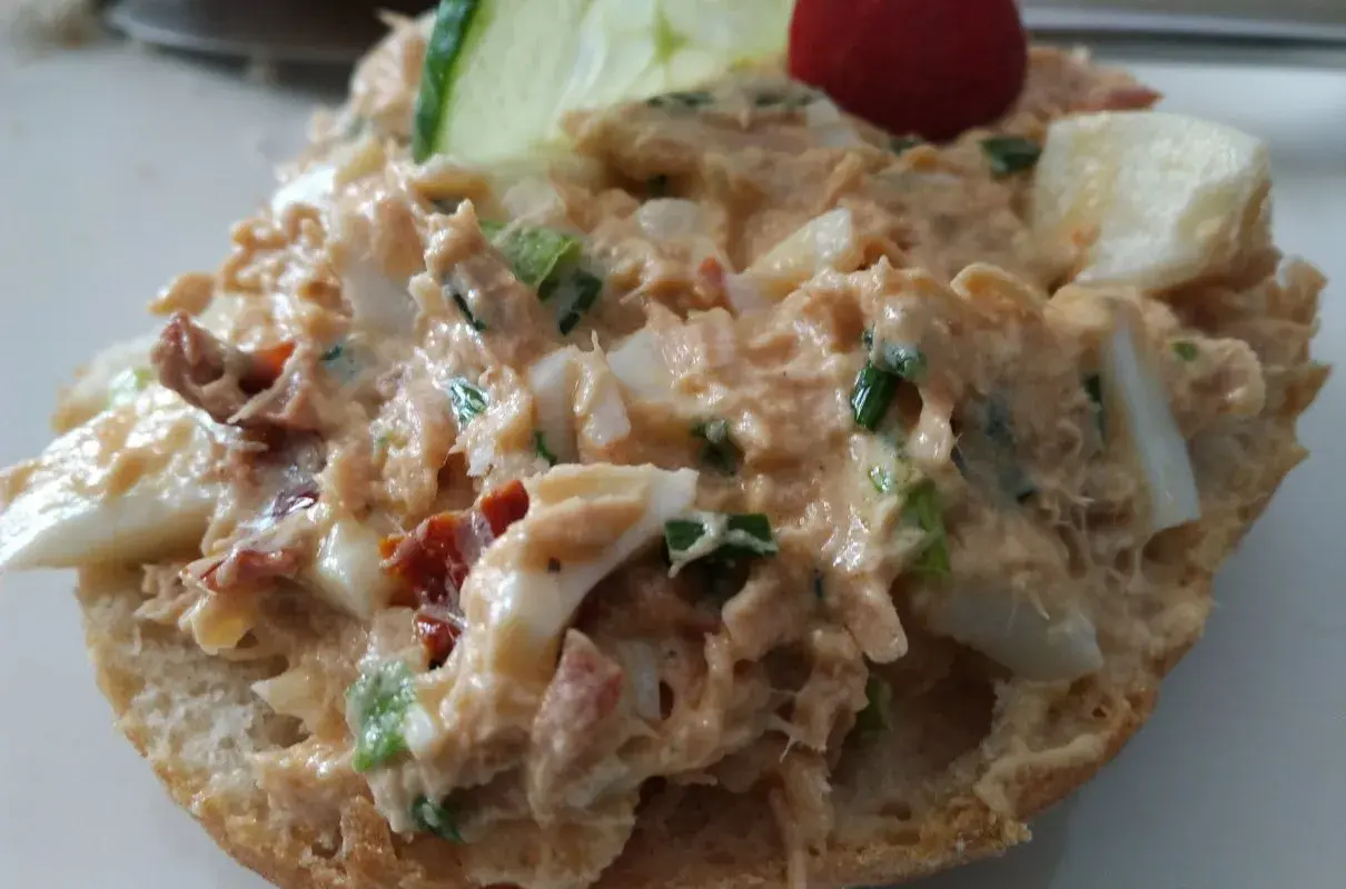 Pyszna pasta z tuńczyka z jajkiem i szczypiorkiem na bułce, ozdobiona plasterkiem ogórka i pomidorkiem.