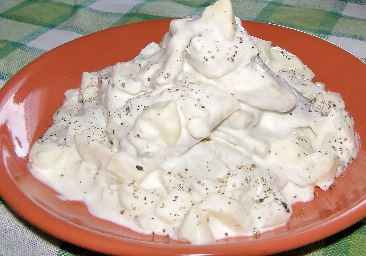 Pyszne śledzie w śmietanie, doprawione pieprzem, na pomarańczowym talerzu.