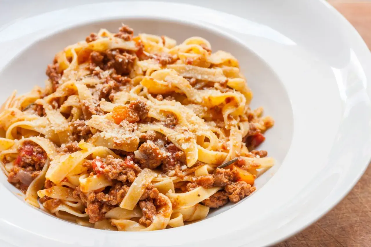 Pyszny makaron tagliatelle z bogatym sosem bolognese, posypany parmezanem. Idealny przepis na obiad.