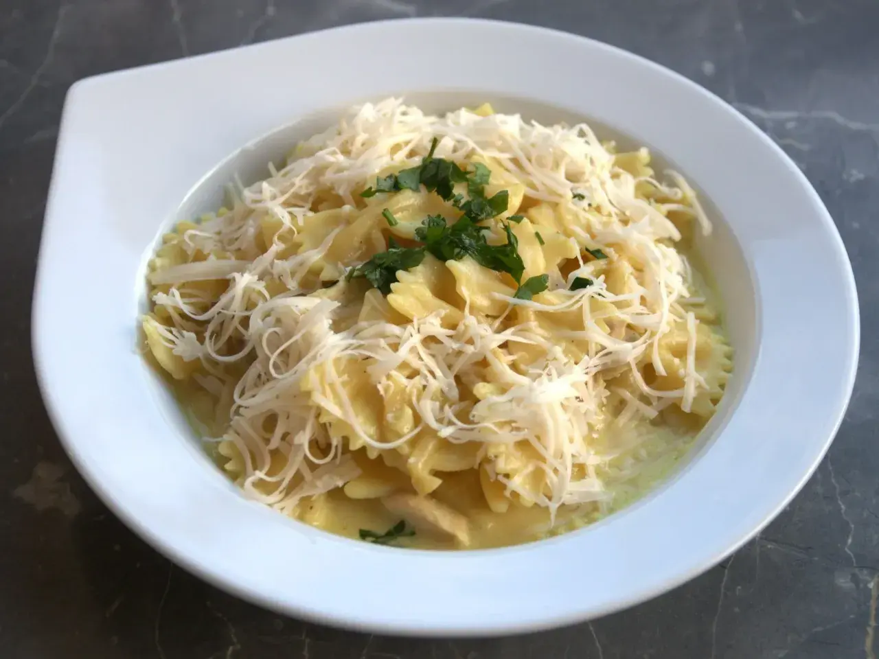 Pyszne farfalle w kremowym sosie z kawałkami gotowanego kurczaka, posypane startym serem i natką pietruszki. Idealny pomysł, co zrobić z gotowanego kurczaka.