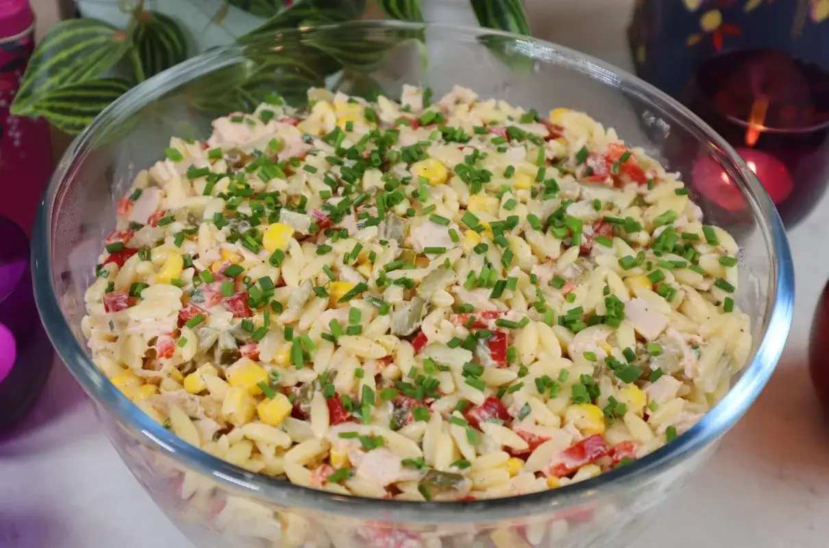 Pyszna sałatka z makaronem orzo, kukurydzą, papryką i kurczakiem, posypana szczypiorkiem. Idealna na letnie dni.
