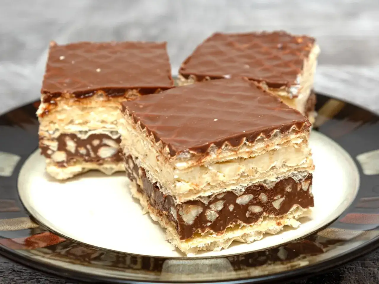 Trzy kawałki wafelka z mlekiem w proszku, przełożone kremem i orzechami, oblane czekoladą.