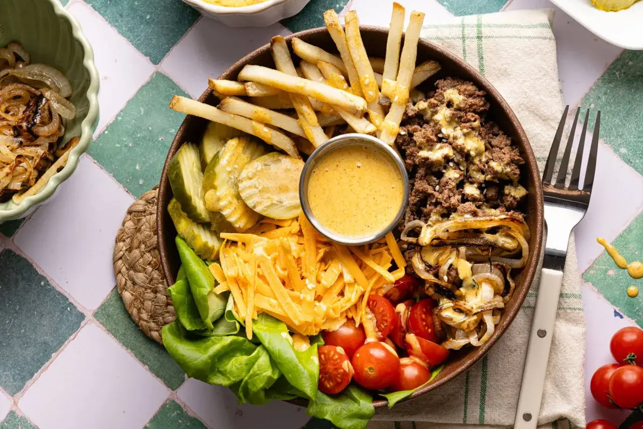 Jak zrobić sos do burger bowl: mięso mielone, frytki, ser, ogórki, pomidorki, sałata i karmelizowana cebulka.