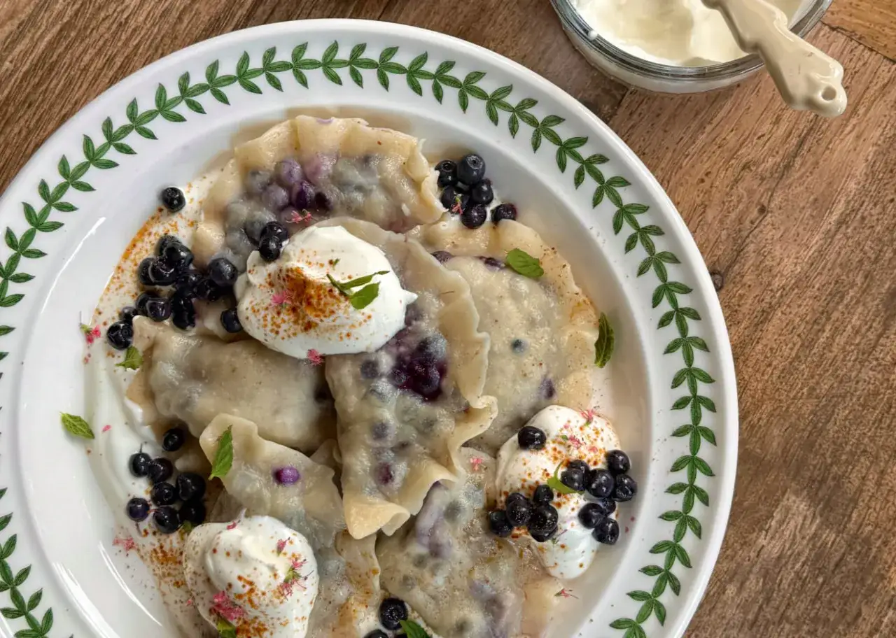 Pyszne pierogi z borówkami, polane śmietaną i posypane świeżymi owocami. Letnia uczta na talerzu.