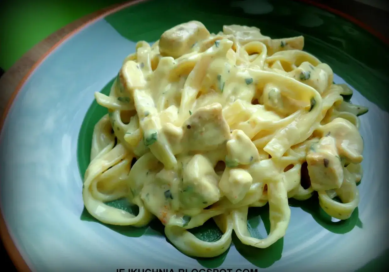 Tagliatelle z kurczakiem w kremowym sosie z serka topionego, posypane ziołami. Pyszne danie na talerzu.