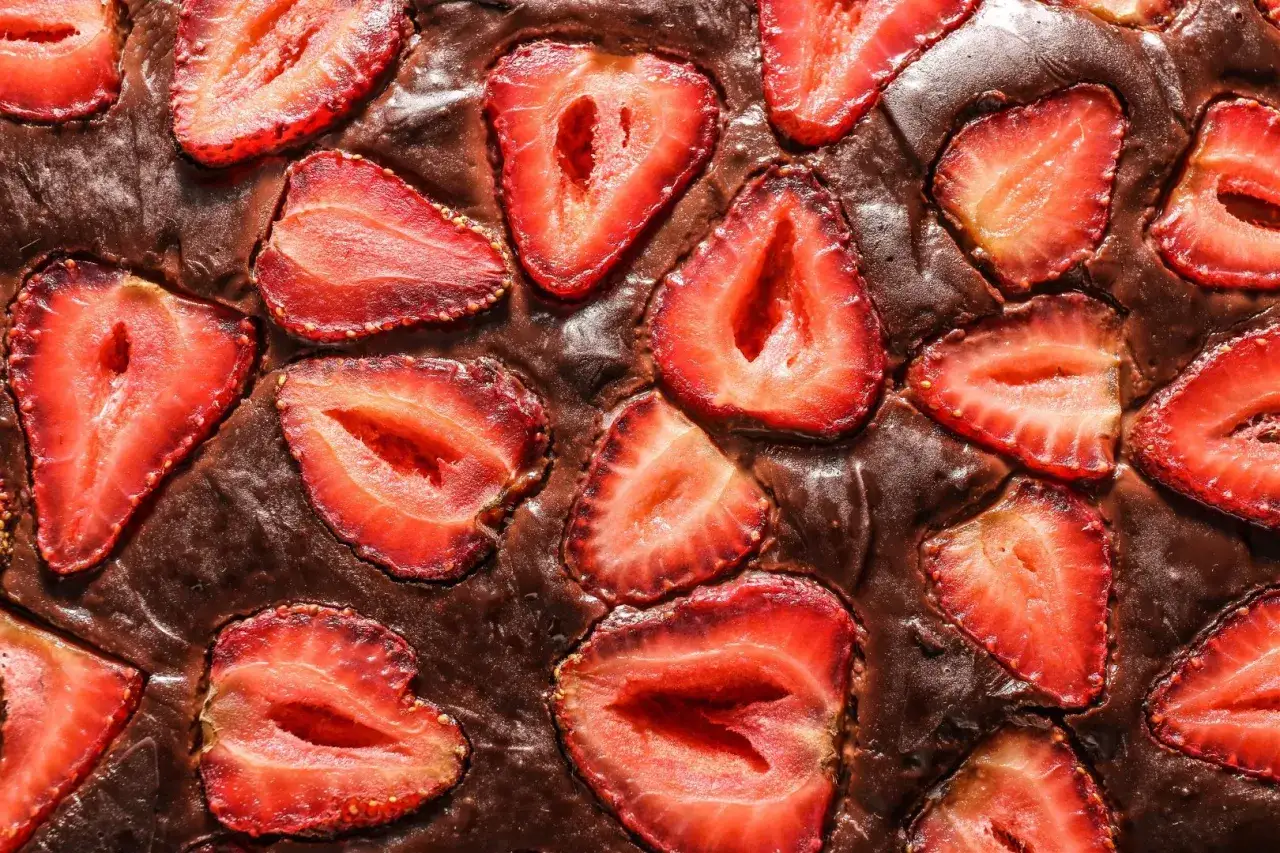 Czekoladowy brownie z kawałkami świeżych truskawek, wyglądające apetycznie i pysznie.